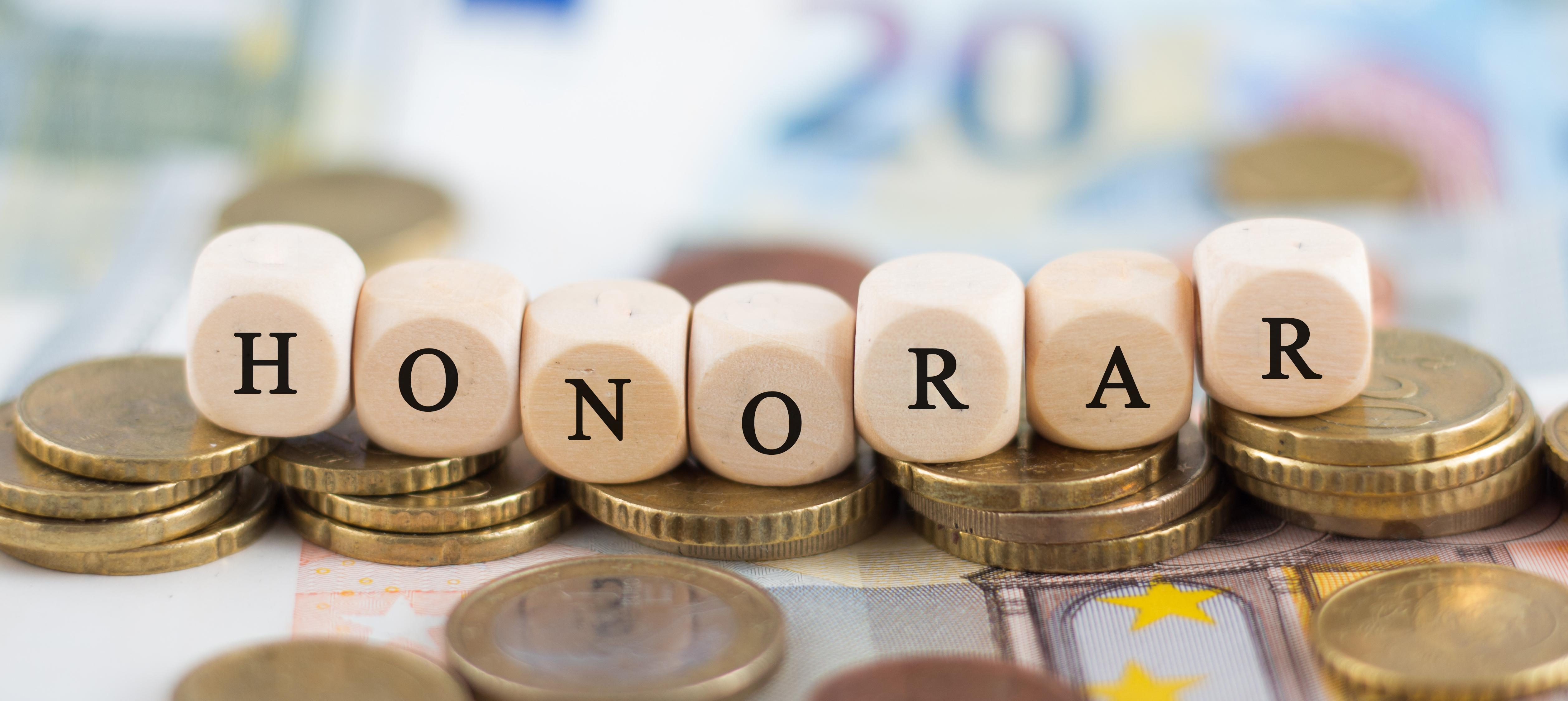 Sieben Würfel mit Buchstaben, die das Wort "Honorar" bilden. Im Hintergrund sieht man Geld.