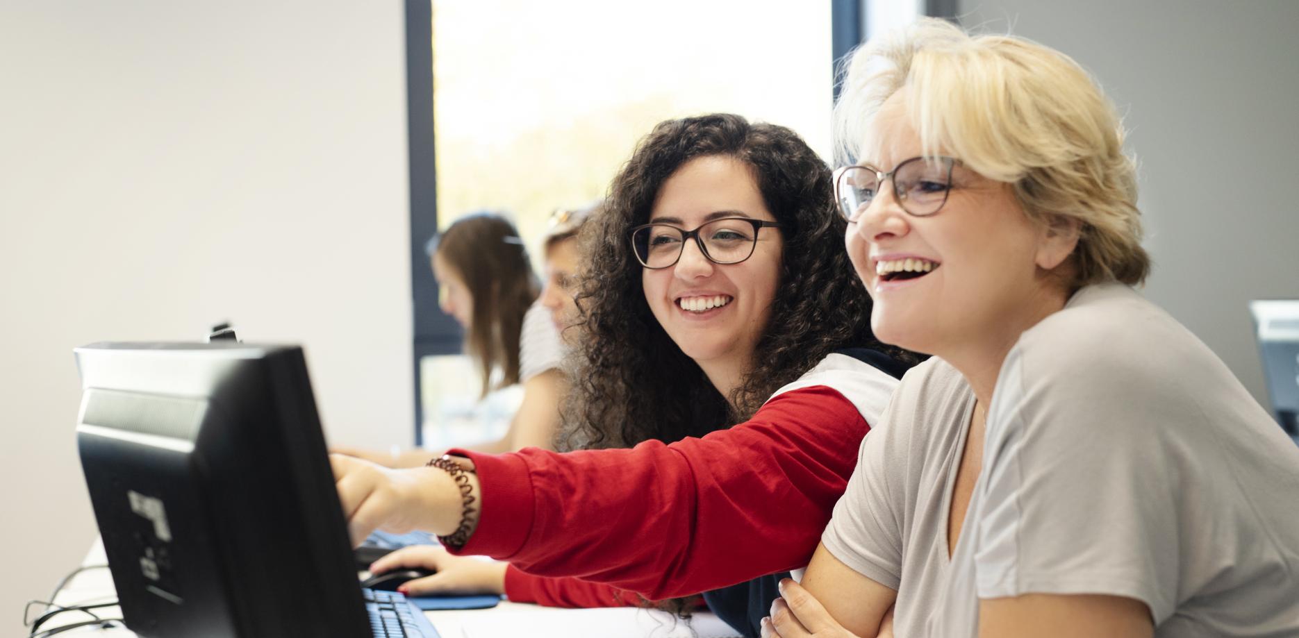 Wei Frauen sitzen vor einem Computer und lachen