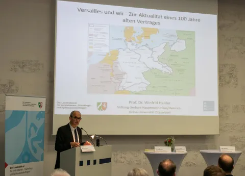 Mann an einem Rednerpult vor einer Leinwand mit Präsentationsunterlagen