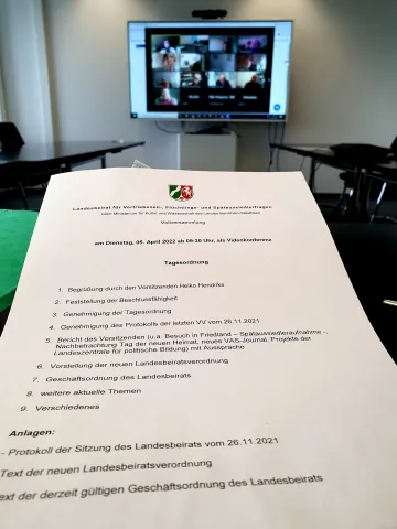 Gedruckte Tagesordnung, im Hintergrund ein Bildschirm
