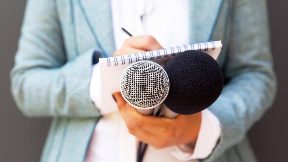 Silhouette einer Reporterin mit gezücktem Block und Mikrofon