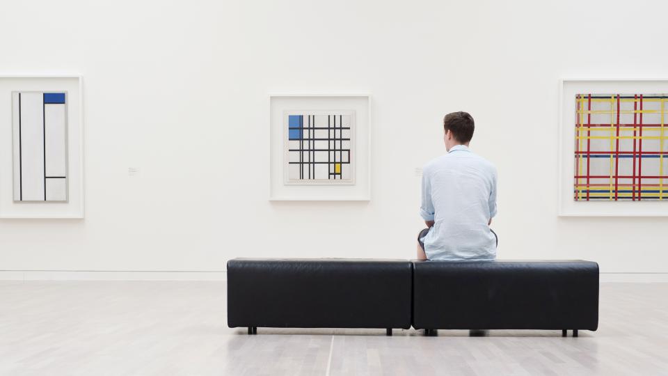 Ein Mann sitzt in einem Museum vor drei Kunstwerken.