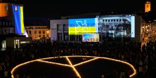 Ein aus Kerzen gelegtes Friedenssymbol auf einem Vorplatz mit der ukrainischen Flagge im Hintergrund