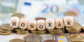 Sieben Würfel mit Buchstaben, die das Wort "Honorar" bilden. Im Hintergrund sieht man Geld.