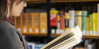 Eine Frau steht vor einer Bücherwand und blättert durch ein Buch.