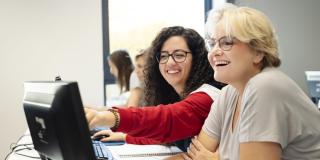 Wei Frauen sitzen vor einem Computer und lachen