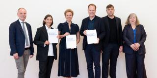 Gruppe auf rotem Teppich vor weißer Wand mit Bericht