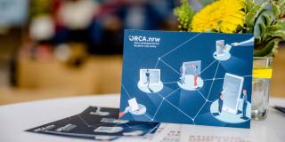 ORCA.nrw-Postkarte auf Tisch mit Blumendeko