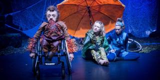 Bühnensituation mit einem Schauspieler im Rollstuhl und zwei sitzenden Schauspielerinnen