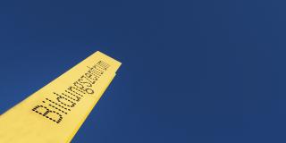 Ein gelbes Schild mit der Aufschrift "Bildungszentrum" ragt in einen blauen Himmel.