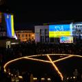 Ein aus Kerzen gelegtes Friedenssymbol auf einem Vorplatz mit der ukrainischen Flagge im Hintergrund
