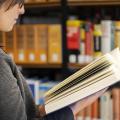 Eine Frau steht vor einer Bücherwand und blättert durch ein Buch.