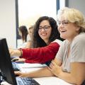 Wei Frauen sitzen vor einem Computer und lachen